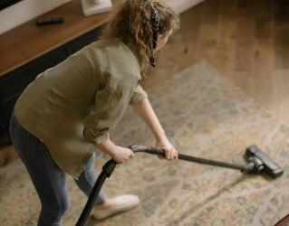 High-angle view of a woman vacuuming a patterned carpet in a stylish living room.